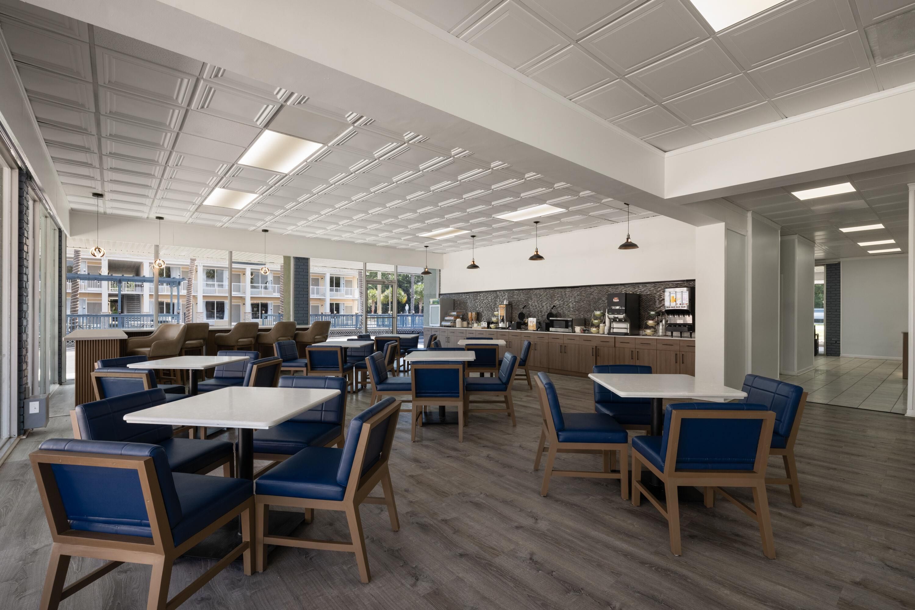 A spacious indoor area with multiple seating arrangements, including tables and chairs, and a kitchen area in the background.
