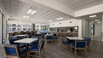A spacious indoor area with multiple seating arrangements, including tables and chairs, and a kitchen area in the background.