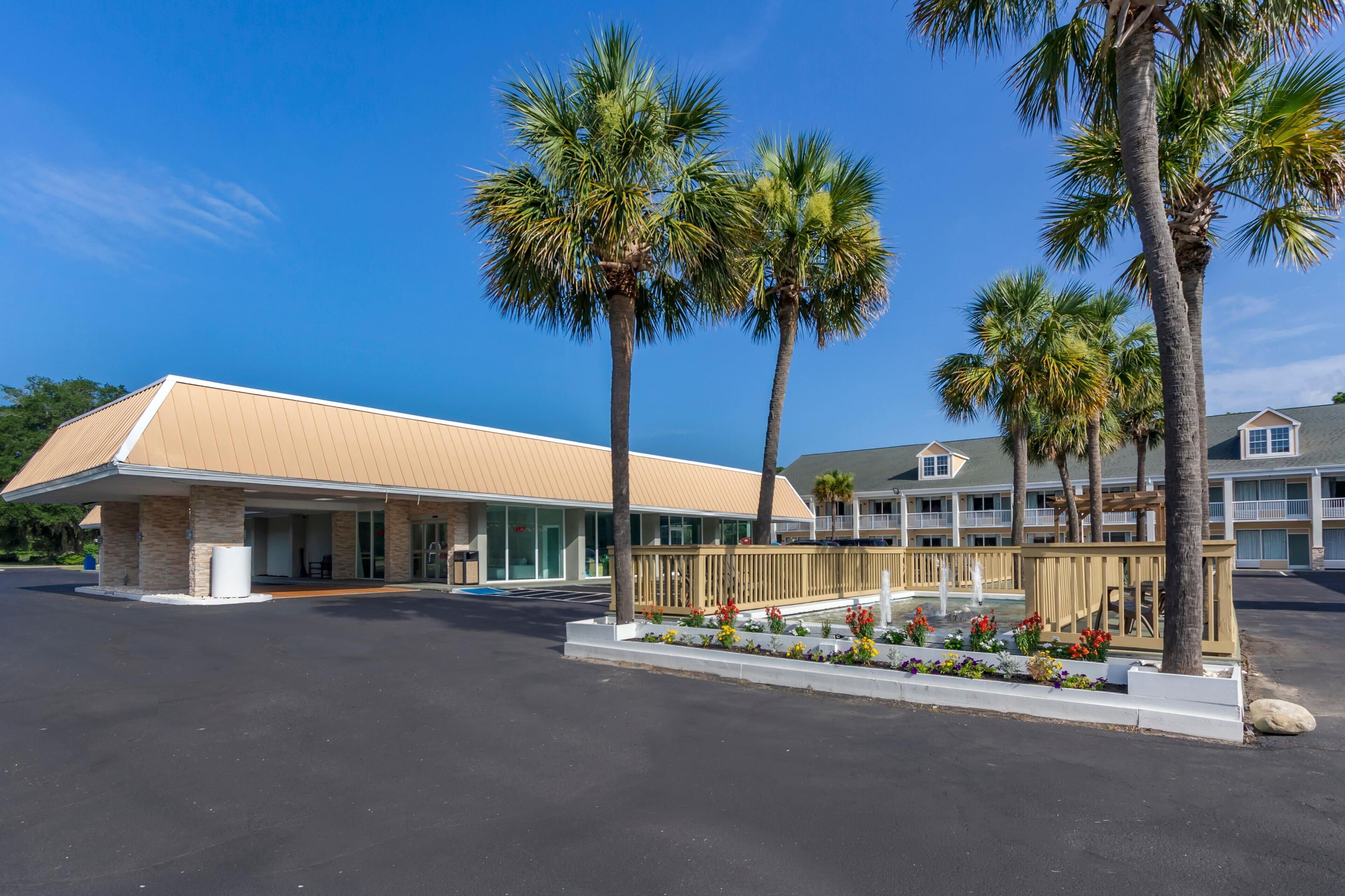 A hotel with a flat-roofed building, a covered outdoor area, and a landscaped garden with a water feature.