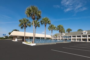 A hotel with a parking lot, palm trees, and a building with a white facade and blue accents.