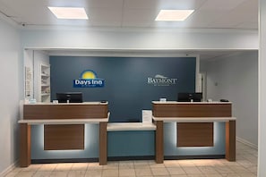 A reception desk with two computer stations, a blue wall with logos of Days Inn and Baymont, and a tiled floor. - Days Inn By Wyndham Pawleys Island (Pawleys Island)