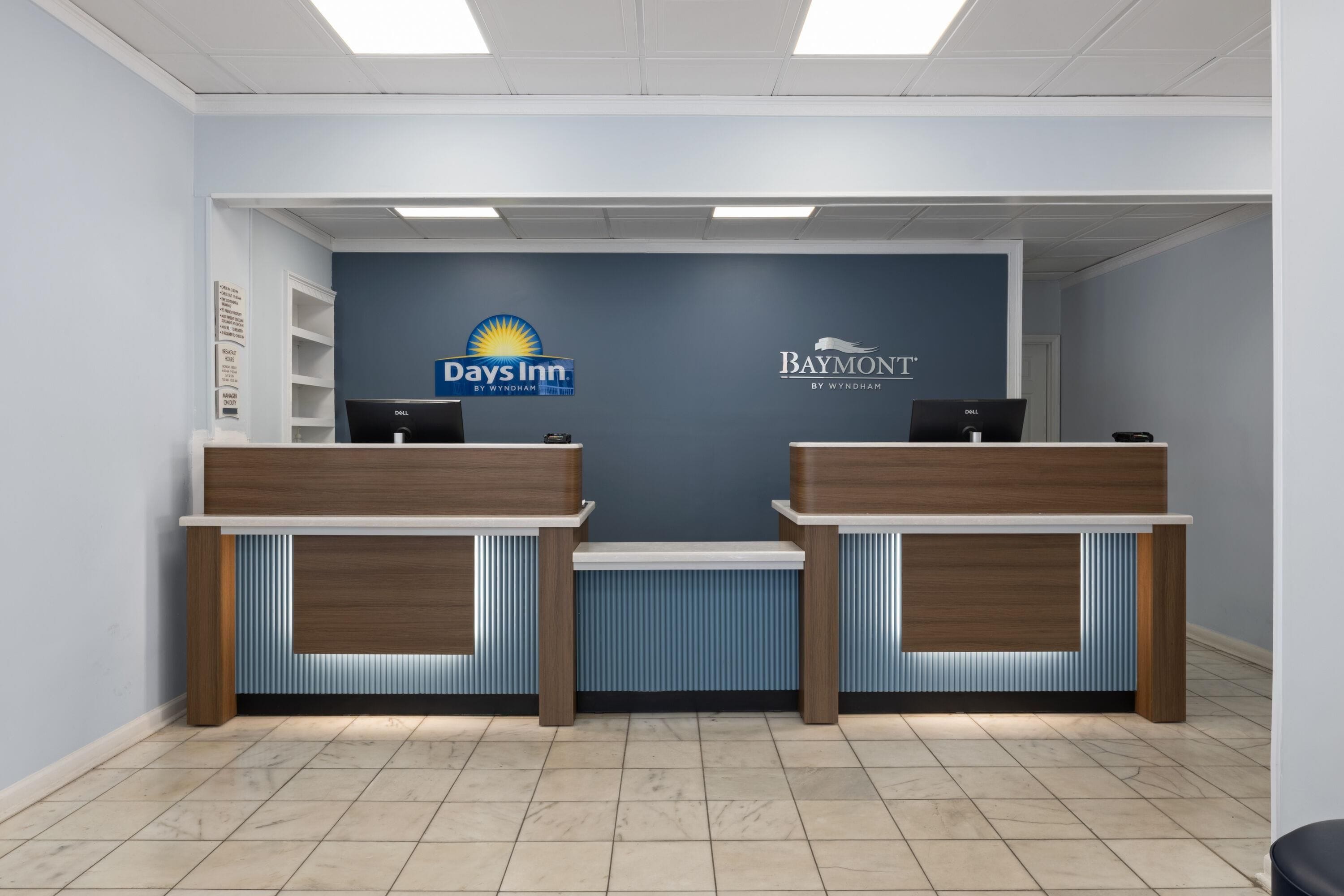 A reception area with two reception desks, a blue wall with logos, and a tiled floor.