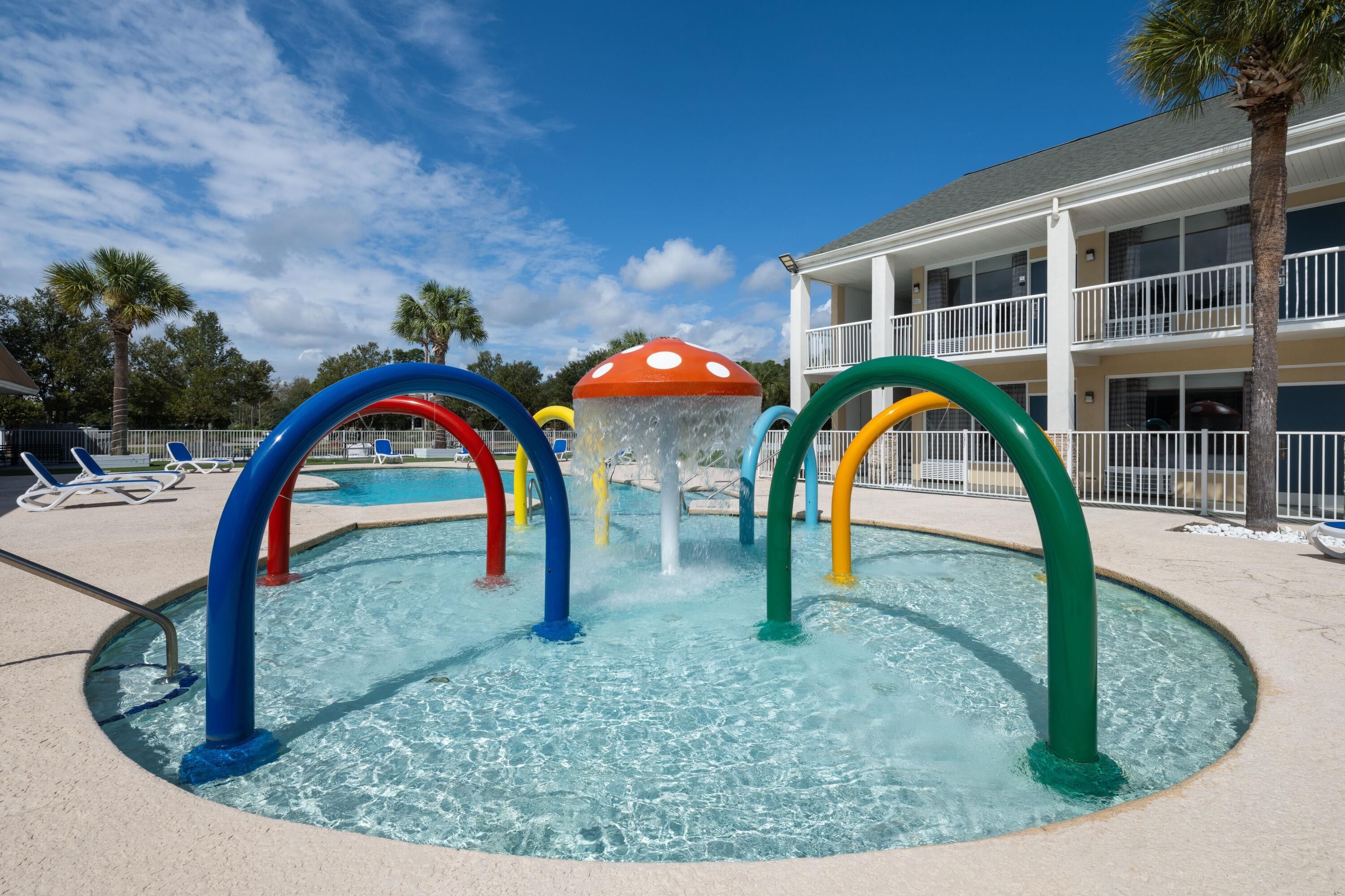 A pool area with a water play structure featuring colorful arches and a mushroom-shaped fountain.