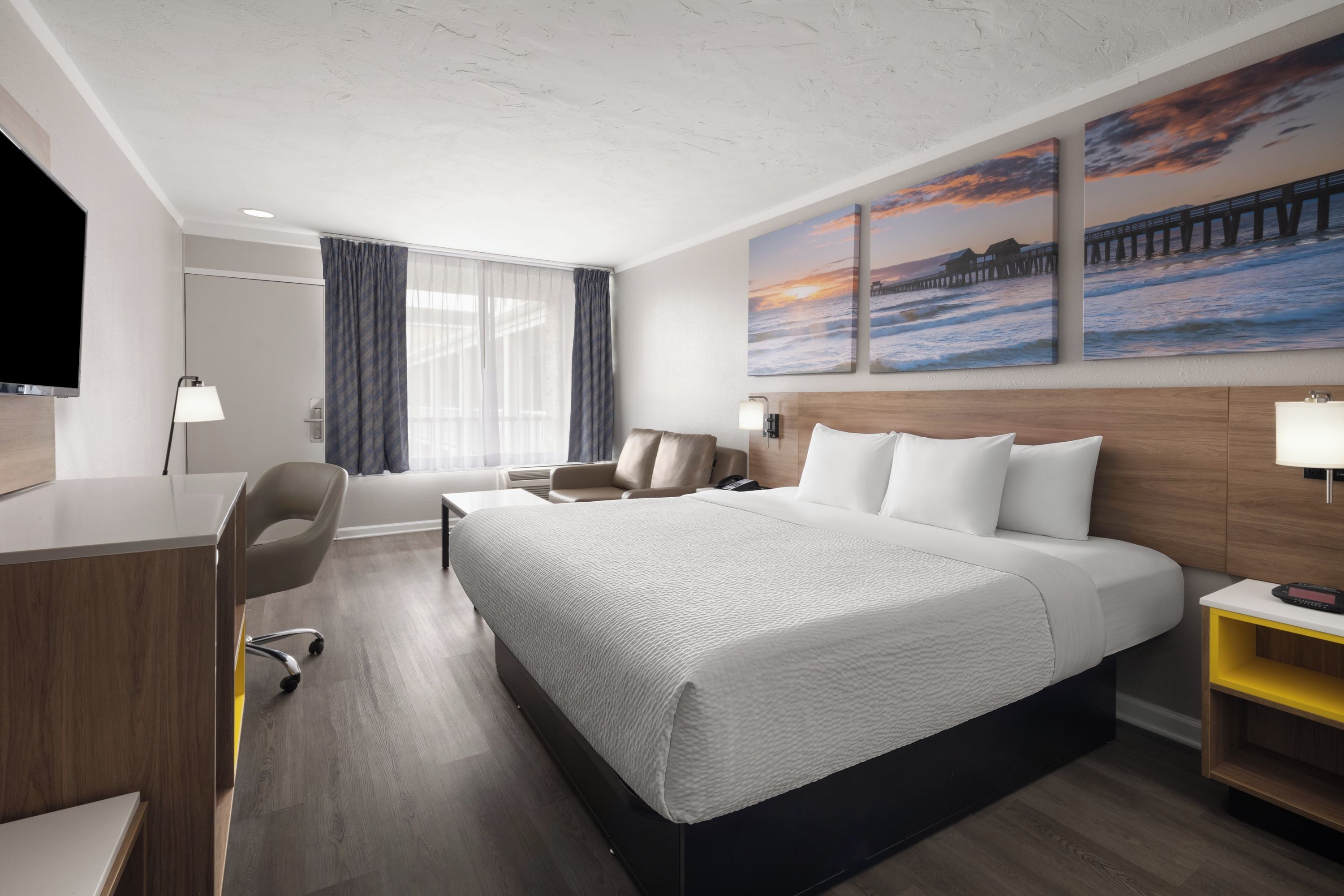 Habitación de hotel con cama, escritorio, silla y una obra de arte en la pared.