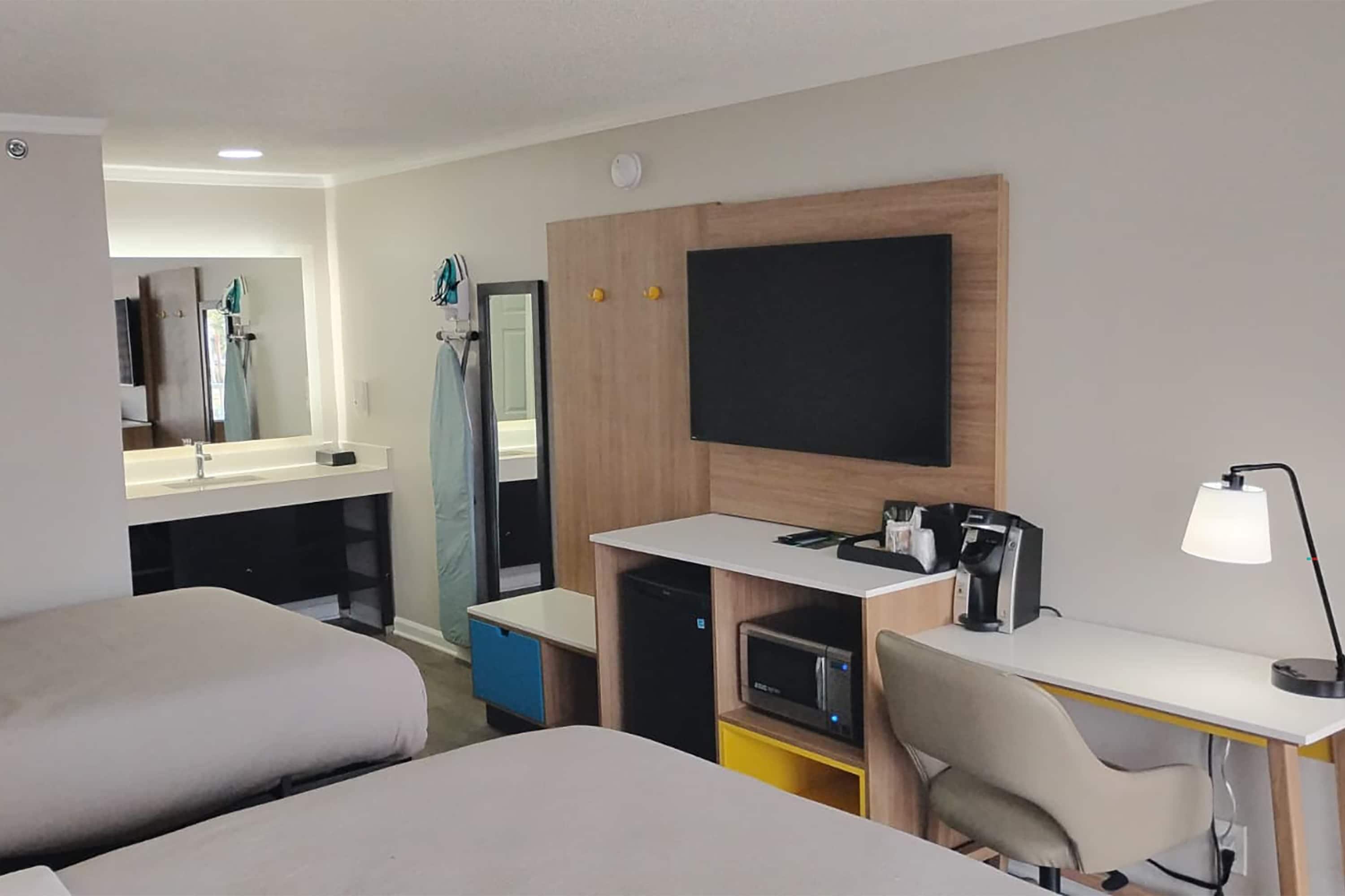 A hotel room with two beds, a desk with a computer, a coffee machine, and a TV.