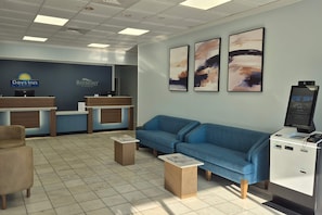 A hotel lobby with a reception desk, a blue sofa, a small coffee table, and a digital kiosk. - Days Inn By Wyndham Pawleys Island (Pawleys Island)