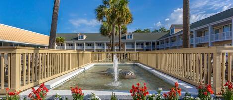 A hotel with a pool, surrounded by a wooden fence, and a palm tree in the center.