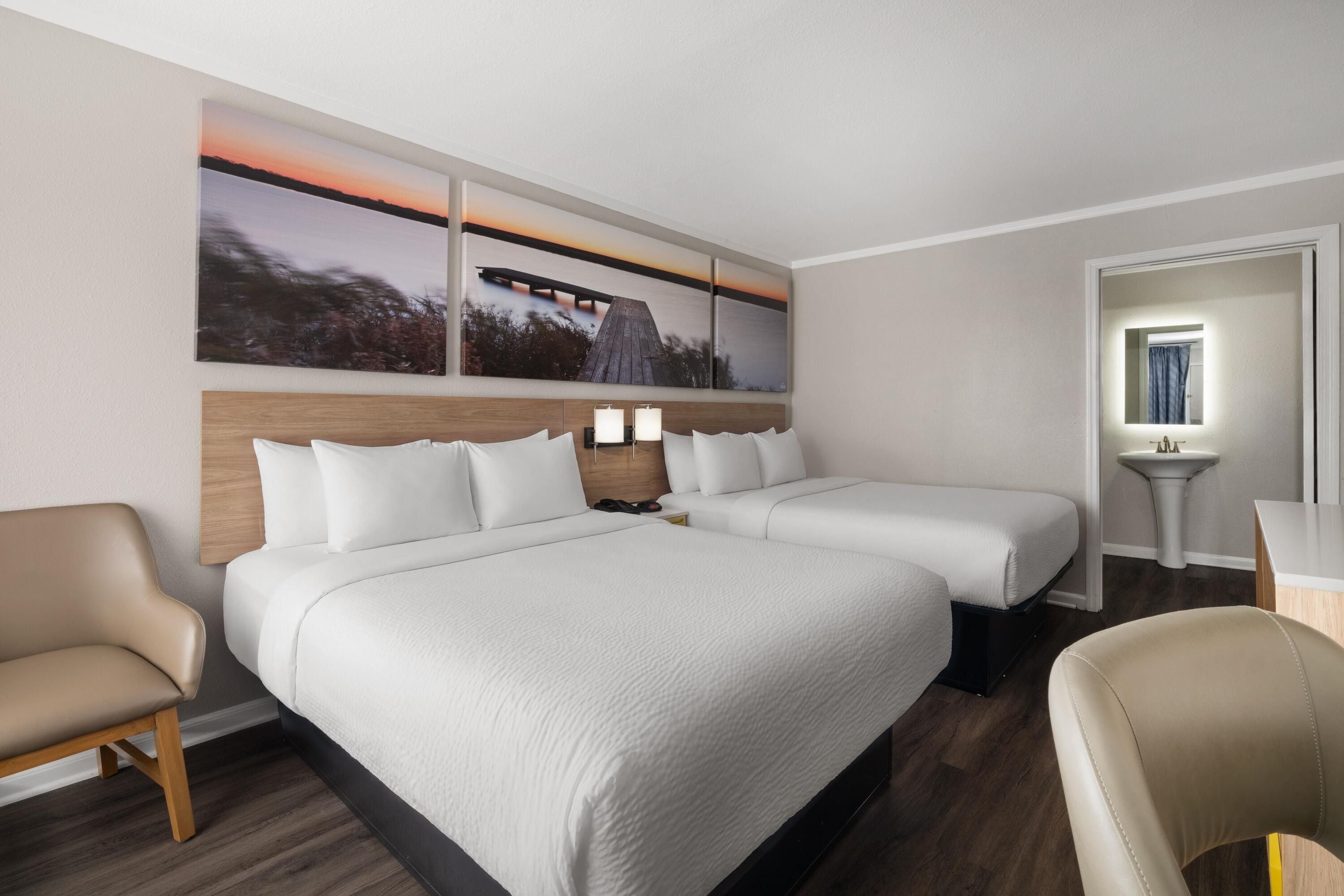 Habitación de hotel con una cama grande, dos mesitas de noche con lámparas, una silla y un baño con lavabo y espejo.