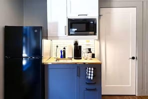 A compact kitchen with a black refrigerator, a microwave, a coffee maker, and a sink. - Danforth Hotel (Toronto)