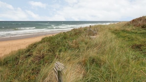 A beach with grassy dunes, a wooden fence, and the ocean in the background. - Viola Cottage (Fraserburgh)