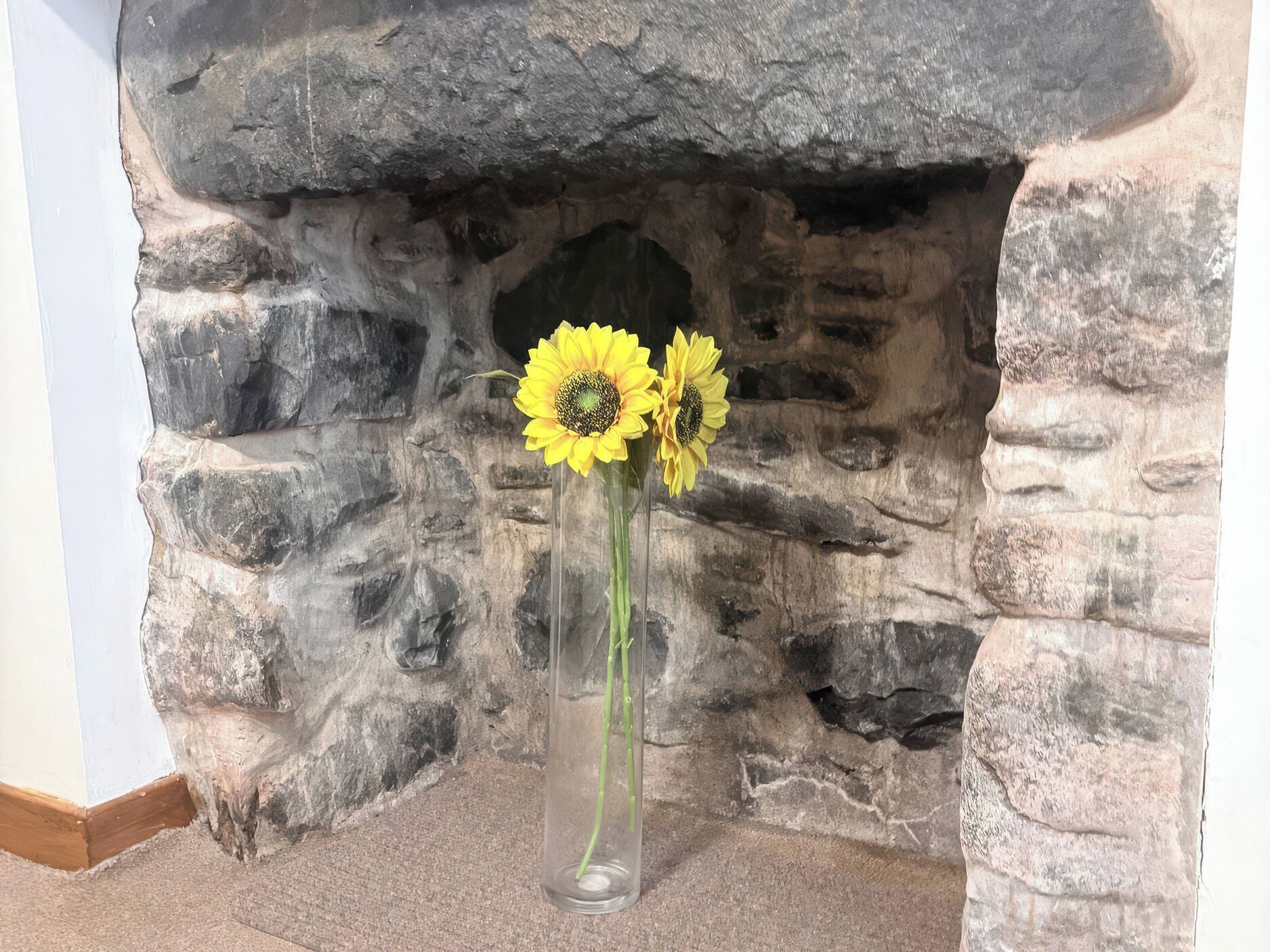 A stone fireplace with a vase of sunflowers.
