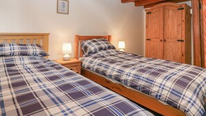 A bedroom with two beds, wooden headboards, nightstands with lamps, a wooden wardrobe, and a framed picture on the wall. - Viola Cottage (Fraserburgh)
