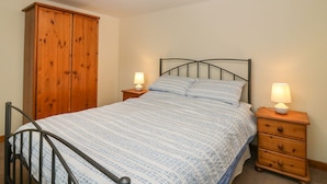 A bedroom with a bed, wooden wardrobe, two bedside tables with lamps, and a metal-framed chair. - Viola Cottage (Fraserburgh)