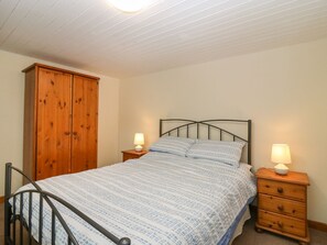 Quarto com cama, guarda-roupa de madeira, duas mesas de cabeceira com luminárias e uma cadeira com estrutura de metal.