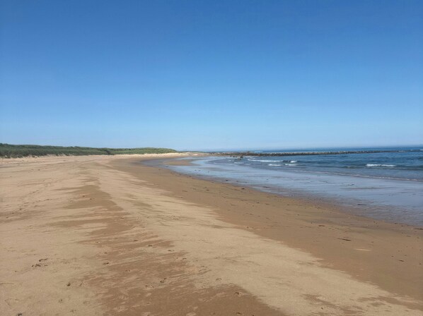 A wide sandy beach with gentle waves, a clear sky, and a distant rocky outcrop.