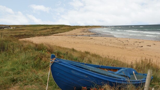 A beach with a blue boat tied to a post, sandy shore, and grassy dunes. - Viola Cottage (Fraserburgh)