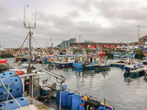 Um porto com vários barcos atracados, um grande edifício industrial ao fundo e um céu nublado.