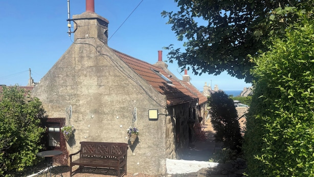 A stone building with a chimney, a bench, and a small garden area. - Viola Cottage (Fraserburgh)