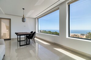 A modern room with a dining table, chairs, a hanging light fixture, and large windows offering a view of the sea and buildings. - Exclusive Luxury Villa Casa Blanca: Private Pool & Stunning Ocean Views (benalmadena)