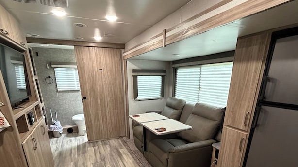 A compact RV interior with a kitchenette, a seating area, and a small table.