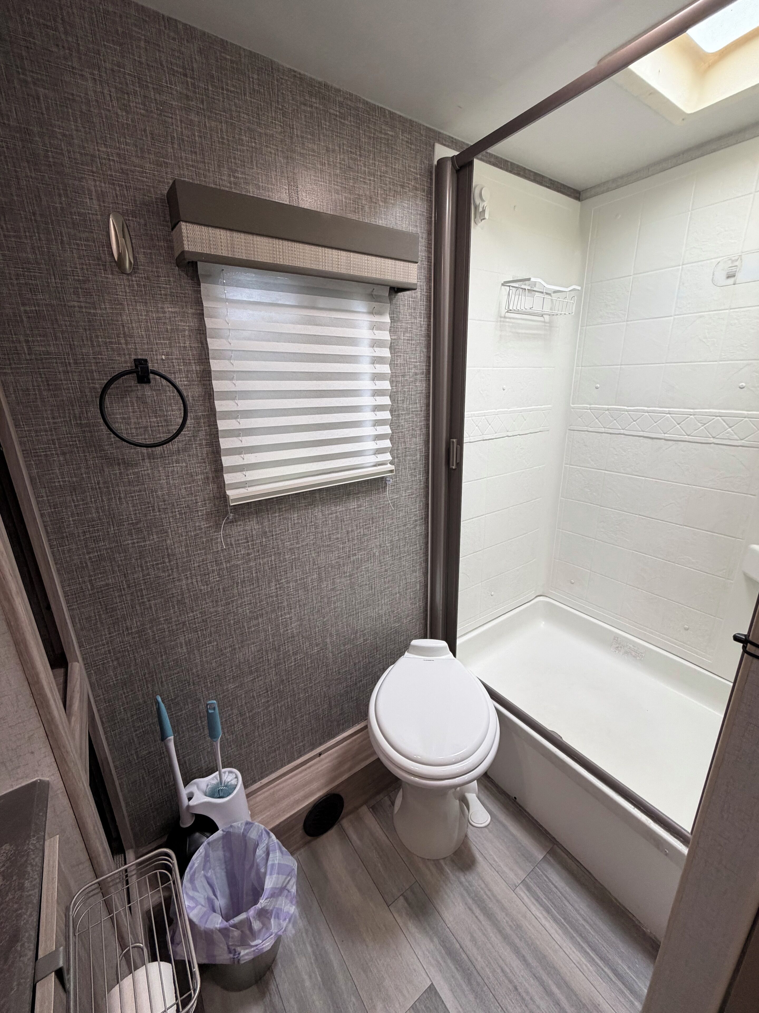 A bathroom with a toilet, a shower, a window with blinds, and a towel rack.