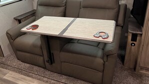 A compact RV interior with a sofa, a small table, and a window with blinds.