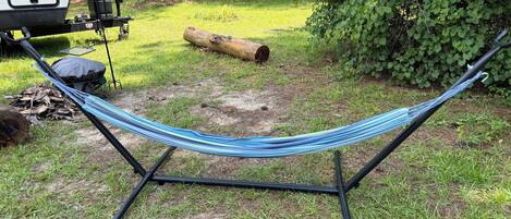 A hammock set up on a stand in a grassy area with a tree and a log nearby.