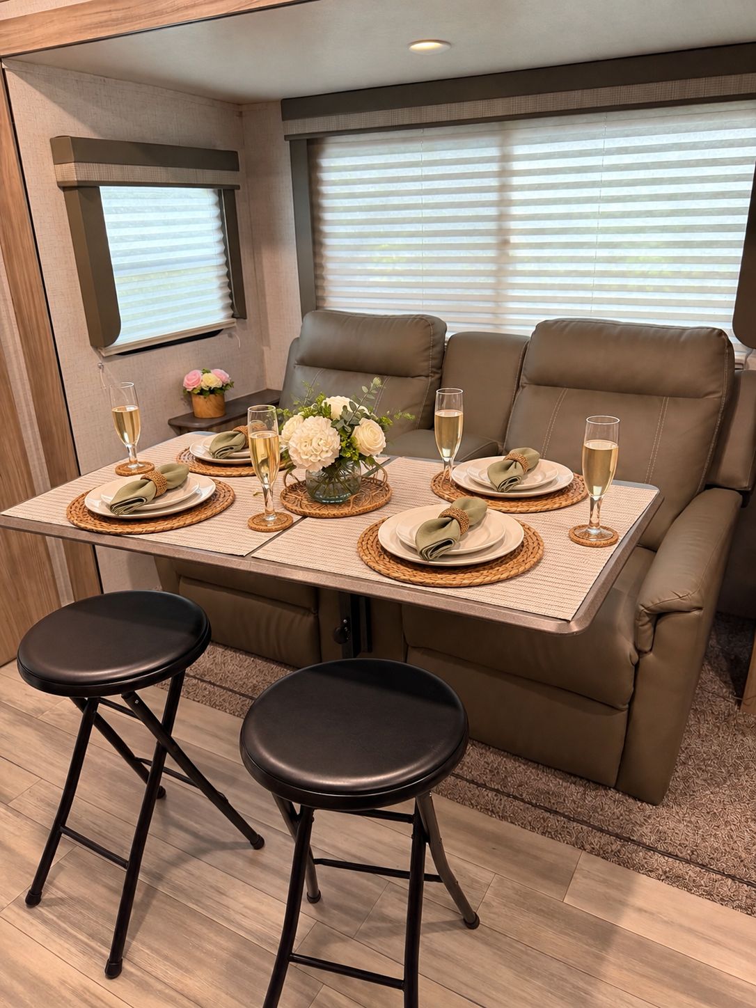 Un coin repas avec une table dressée pour deux personnes, deux tabourets et un canapé à deux places.