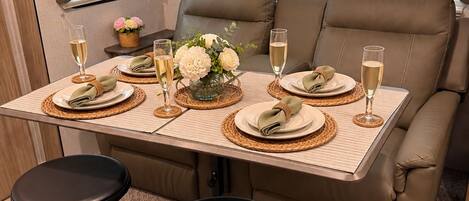A dining area with a table set for two, two stools, and a sofa with two seats.
