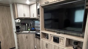 A modern kitchen with wooden cabinets, a built-in oven, a microwave, and a large flat-screen TV.