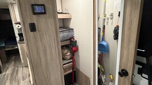 A hotel room with a wooden door, a digital thermostat, a blue mat, and a mop on the wall.