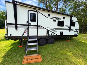 A recreational vehicle named 'MINNIE' with a step-up platform and a welcome mat.