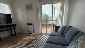 Ein Wohnzimmer mit einer Couch, einem Couchtisch, einem Fernseher und einer Glastür, die auf einen Balkon führt.