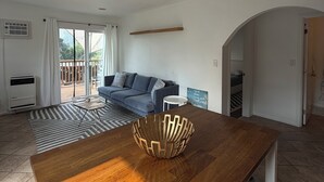 Ein großzügiger Wohnbereich mit Holztisch, Deckenventilator, blauem Sofa und einer Glastür zum Balkon.