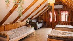 Une pièce mansardée chaleureuse avec des poutres en bois, deux lits avec une literie à motifs, un canapé et des plantes suspendues.