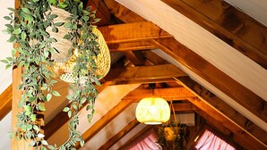 Une chambre confortable située dans les combles, avec des poutres en bois, une télévision, deux lits et une plante suspendue.