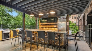 Un espace bar extérieur équipé d’un barbecue, de sièges et d’un panneau indiquant « INTERDICTION DE VERRE ».