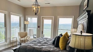 Un dormitorio con una cama grande, una silla, una mesita de noche y vistas al exterior a través de amplias ventanas.