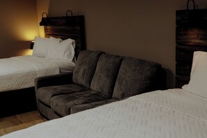 A hotel room with two beds, a sofa, and a nightstand with a lamp. - Enjoy a cozy stay at U.P. Trails Getaway in the  Tahquamenon Room (Eckerman)
