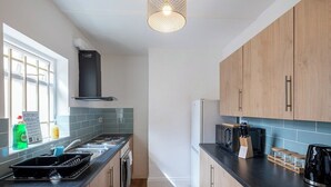 Una cocina moderna con armarios de madera, encimera negra, horno empotrado y una lámpara colgante.