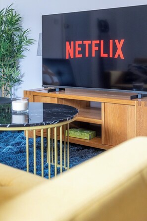 A modern living room with a flat-screen TV, a wooden entertainment unit, a glass coffee table, and a blue carpet. - Spacious 2BR APT - Sleeps 5 - Private Parking (Somerset)
