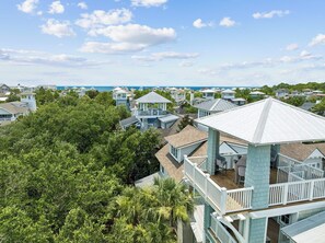 A coastal residential area with multiple houses, some with elevated structures and balconies, surrounded by lush greenery. - Gulf Views, Private Pool and Golf Cart (Watersound)