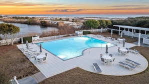 A swimming pool with lounge chairs and tables, surrounded by a white fence, with a view of the ocean and a sunset. - Gulf Views, Private Pool and Golf Cart (Watersound)