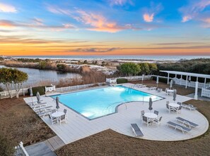 A swimming pool with lounge chairs and tables, surrounded by a white fence, with a view of the ocean and a sunset. - Gulf Views, Private Pool and Golf Cart (Watersound)