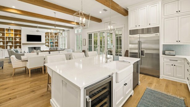 A modern kitchen with a central island, white cabinetry, stainless steel appliances, and a dining area with white furniture. - Gulf Views, Private Pool and Golf Cart (Watersound)