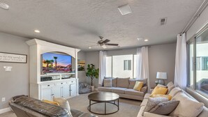 A living room with a flat-screen TV, a ceiling fan, a sofa, a coffee table, and a window with curtains.