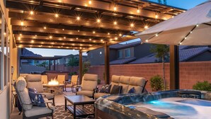 An outdoor patio with a hot tub, seating, and string lights.
