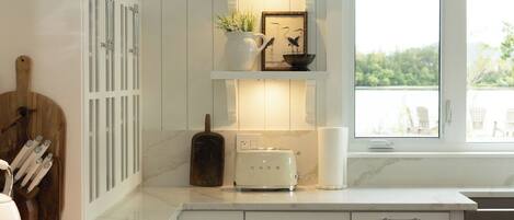 A modern kitchen with white cabinetry, a built-in stove, and a window overlooking a natural landscape.