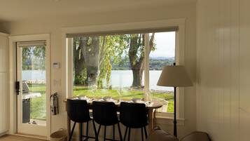 A dining area with a table set for four, overlooking a lake with trees and a distant view of a town.
