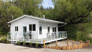 A small, single-story cabin with a balcony, surrounded by trees.
